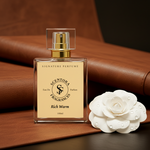 Perfume bottle with gold cap and beige label on a brown leather surface next to a white flower.
